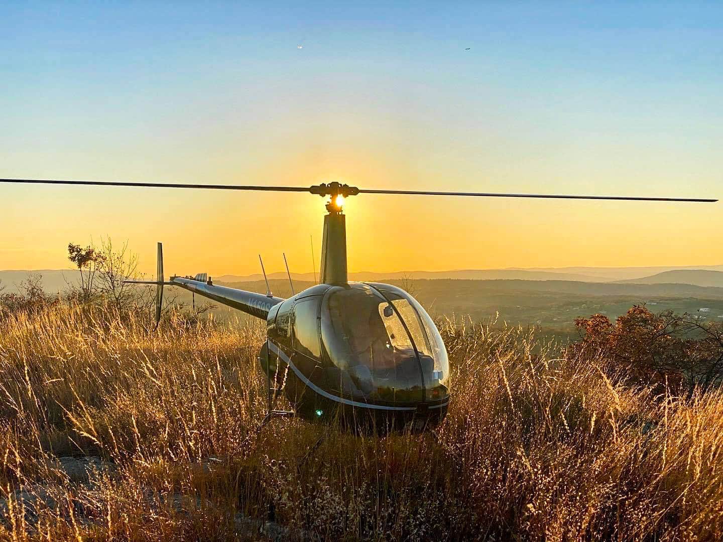 helicopter landed on a hillside with sunset and mountains in the background